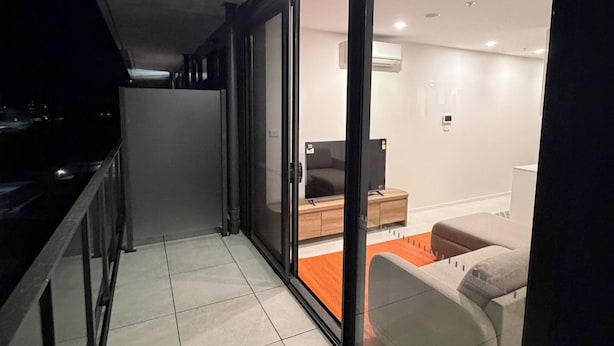 A corridor with a sliding glass door leading to a modern living area with a sofa and a coffee table. - Brand new G6 apartment (Gungahlin)
