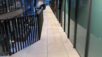 A corridor with glass partitions, a tiled floor, and a railing on one side.