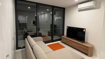 A modern living room with a sofa, a flat-screen TV, and an air conditioning unit.