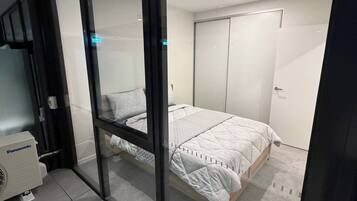 A bedroom with a bed, a wardrobe, and a Panasonic air conditioner.