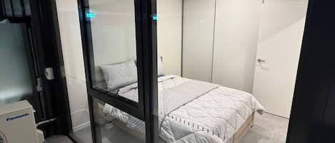 A bedroom with a bed, a wardrobe, and a Panasonic air conditioner.