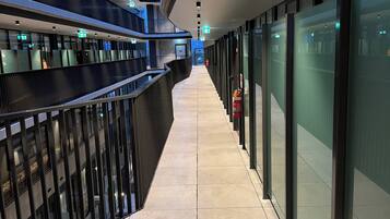 A corridor with glass walls, emergency exit signs, and a tiled floor.