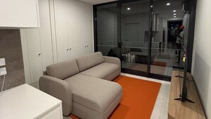 A modern living room with a sectional sofa, a white cabinet, and a glass door leading to a balcony. - G6 Gungahlin brand new (Gungahlin)