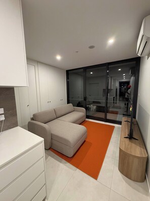 Een moderne woonkamer met een hoekbank, een witte kast en een glazen deur die leidt naar een balkon.