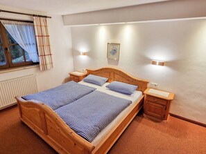 A double bed with a wooden frame, two bedside tables, a window with curtains, and wall-mounted lights. - Hohe salve by Interhome (Hopfgarten im Brixental)