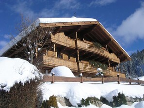 Una xalet de fusta amb un balcó, envoltat de terreny i arbres coberts de neu.