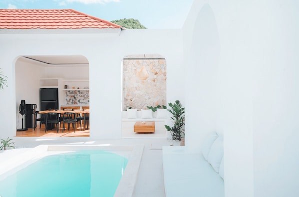 A modern outdoor pool area with a dining space and a kitchen visible through an archway.