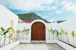A courtyard with a wooden door, white walls, and a tiled floor.