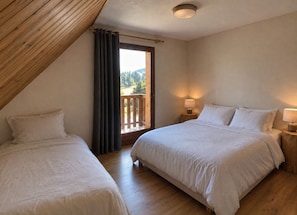 Une chambre avec deux lits, un plafond en bois, un balcon avec vue et une table de chevet avec une lampe.