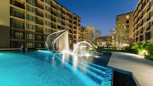 Una piscina con un moderno elemento acuático, rodeada de edificios de varios pisos con balcones.