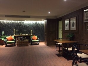Um quarto com piso de tijolos, um sofá verde com almofadas laranja, uma mesa de madeira e uma parede com textura.