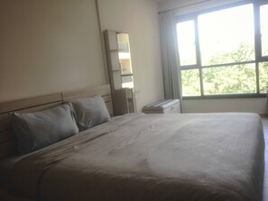 A hotel room with a large bed, a nightstand, a mirror, and a window with a view of trees.