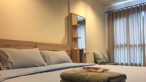 Una habitación de hotel con una cama grande, un cabecero de madera, una mesita de noche, un espejo, una silla y una ventana con cortinas.