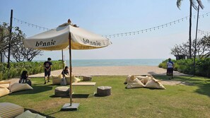 An outdoor seating area with striped cushions and a large umbrella with 'bonnie' branding, overlooking a beach.
