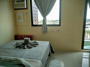A bedroom with a bed, a radiator, a window with curtains, and a view of buildings outside. - Royal Oceancrest Mactan 1BR (Lapu-Lapu)