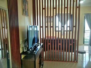 A room with a television on a stand, a window with curtains, and a wooden partition. - Royal Oceancrest Mactan 1BR (Lapu-Lapu)