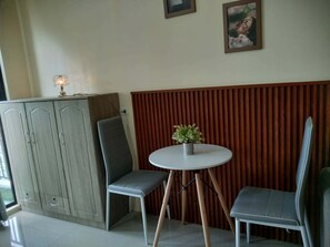 Habitació d'angle amb un armari gris, dues cadires grises, una taula rodona petita amb una planta i una paret de llistons de fusta.