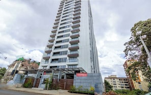 Un immeuble résidentiel à plusieurs étages, doté de balcons, d’une entrée sécurisée et d’un panneau indiquant les appartements disponibles à la vente.
