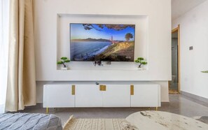 A modern living room with a flat-screen TV mounted on a white wall, a white entertainment unit below, and two small potted plants on either side. - Nairobi City -KilimaNi Next to Junction Mall (Nairobi)
