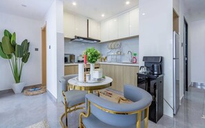 A modern kitchen with white cabinets, a coffee machine, and a dining area with two chairs and a table. - Nairobi City -KilimaNi Next to Junction Mall (Nairobi)