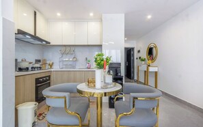 A modern kitchen with white cabinets, a dining area with two chairs and a table, and a mirror on the wall. - Nairobi City -KilimaNi Next to Junction Mall (Nairobi)
