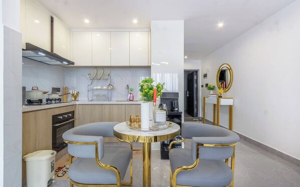 Une cuisine moderne avec des meubles blancs, un coin repas comprenant deux chaises et une table, et un miroir accroché au mur.