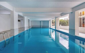 Ein großer, überdachter Pool mit klarem, blauem Wasser, umgeben von weißen W änden und Säulen, mit Blick ins Freie.