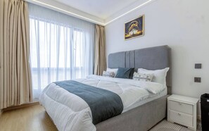 Ein modernes Schlafzimmer mit einem großen Bett, einem Nachttisch, einer Wandsteckdose und einem Fenster mit Vorhängen.