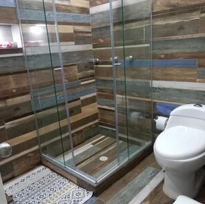 Une salle de bain avec une douche à parois de verre, des toilettes et un tapis à motifs.