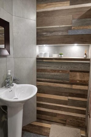 A bathroom with a white sink, a mirror, and a wooden wall with a shelf above it. - Casa Hotel Sweet Home Apt 203 Grupos (Medellín)