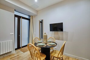 A dining area with a round table, four chairs, a television mounted on the wall, and a window with curtains. - Superb Apartment 1 Bedroom Center of Paris by Studio Prestige (Paris)