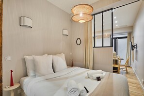 A modern hotel room with a bed, bedside tables, a hanging light fixture, and a view of the dining area. - Superb Apartment 1 Bedroom Center of Paris by Studio Prestige (Paris)