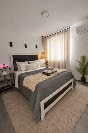 Ein modernes Schlafzimmer mit Bett, Nachttischen, einer Lampe und einer Topfpflanze.