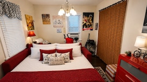 A bedroom with a large bed, a red dresser, a bicycle, and various wall art. - RED ROOM DE Spa Access (Dover)