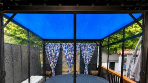 A circular outdoor seating area with a round table and a bench, surrounded by a wooden deck and a blue canopy. - RED ROOM DE Spa Access (Dover)