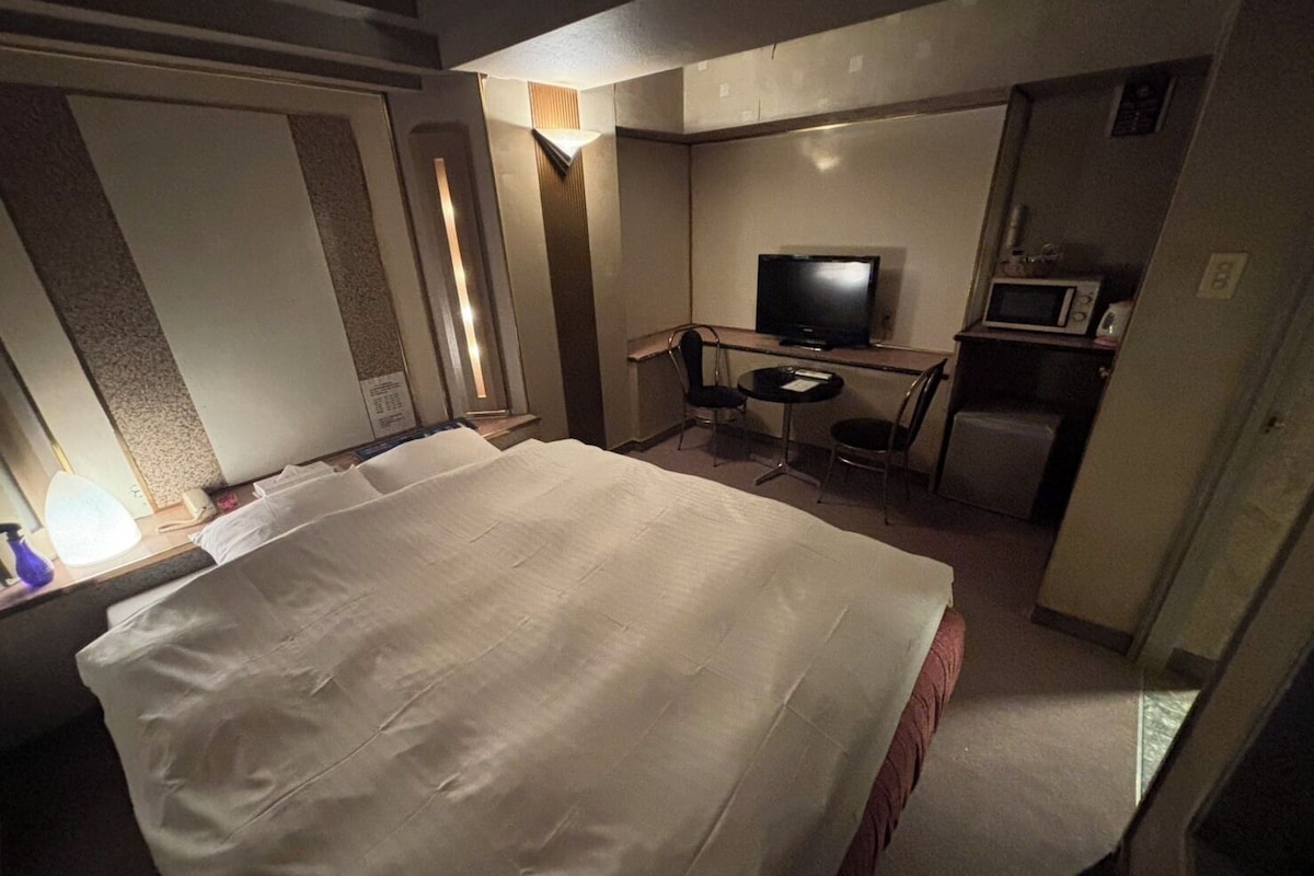 A hotel room with a large bed, a television, a small desk with a chair, and a microwave.