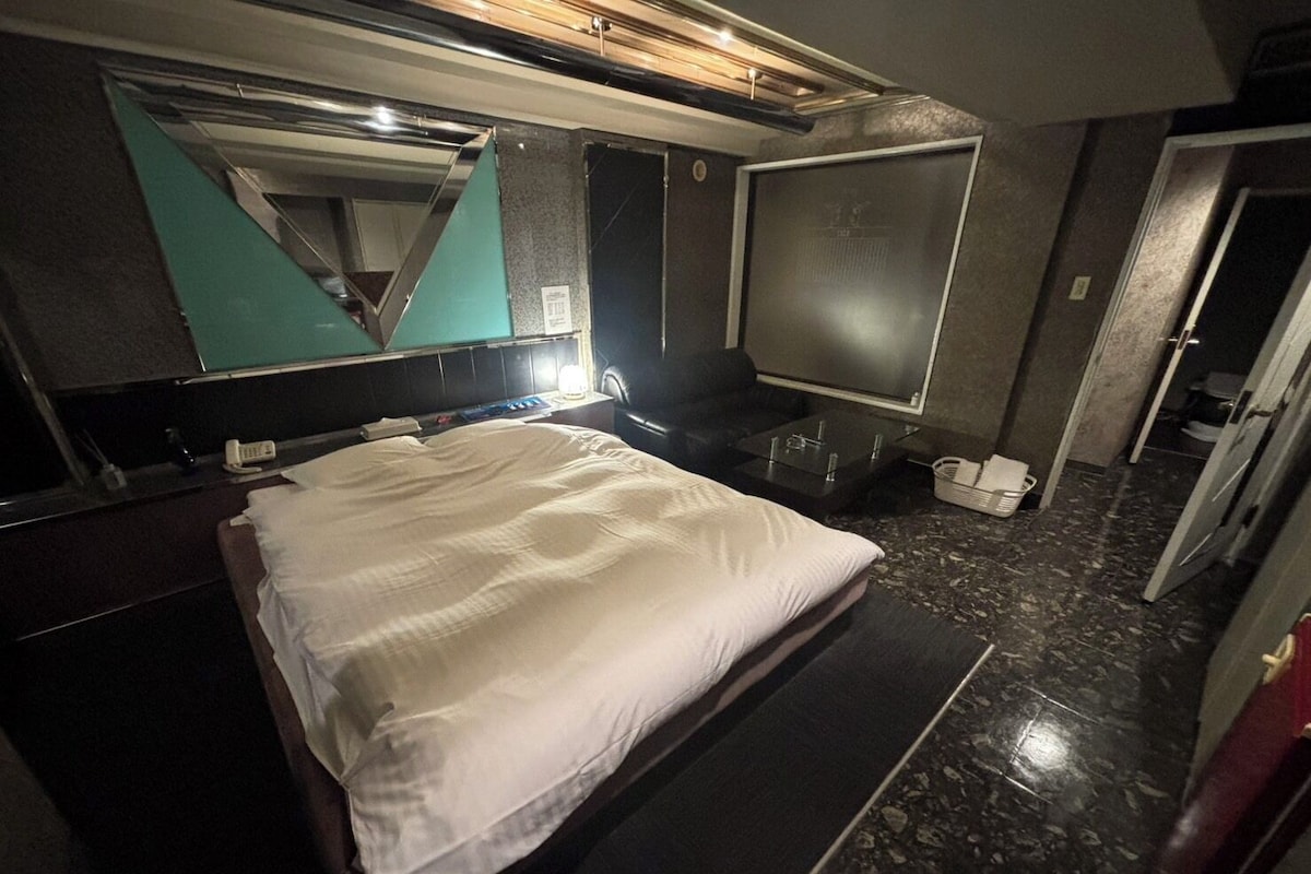 A hotel room with a bed, a large mirror, a television, and a bathroom.