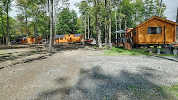 Un terrain de camping doté de plusieurs cabanes en bois, de sentiers de gravier et bordé par une forêt.