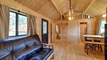 L’intérieur d’une cabane est aménagé avec un canapé en cuir, des murs en bois, un coin repas et une petite cuisine.