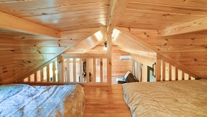 Ein Schlafzimmer im Dachgeschoss mit Holzbalken, einem Bett, einem Schreibtisch und einem Fenster.