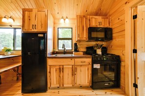 A compact kitchen with wooden cabinetry, a refrigerator, a microwave, and a stove.