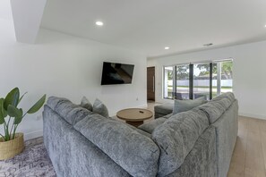 A modern living room with grey upholstered sofas, a round wooden coffee table, and a flat-screen TV mounted on the wall. - Waterfront Hollywood Oasis w/ Private Pool! (Hollywood)