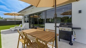 An outdoor patio with a wooden table and chairs, two large umbrellas, a barbecue grill, and a glass-enclosed patio area. - Waterfront Hollywood Oasis w/ Private Pool! (Hollywood)