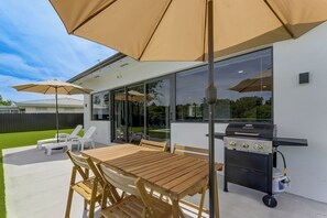 Eine Außenpatio mit Holztisch und -stühlen, zwei großen Sonnenschirmen, einem Grill und einem überdachten Patio-Bereich.