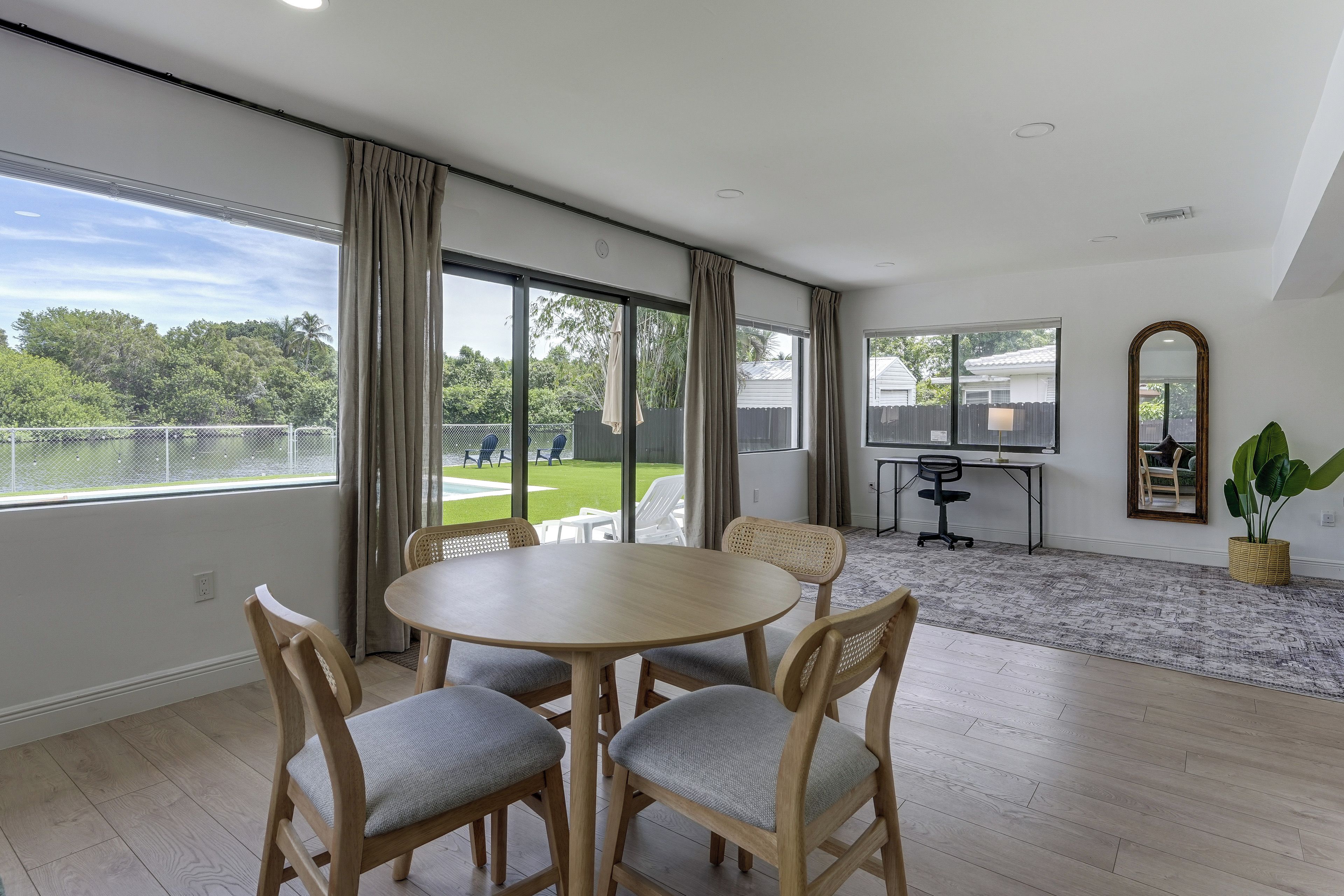 Habitación amplia con una gran mesa redonda y sillas, vista a un patio trasero con piscina y un comedor con vistas a casas vecinas.