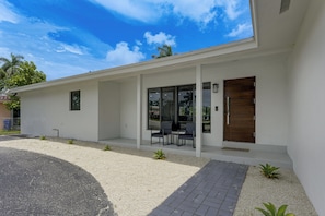 Ein modernes Haus mit überdachter Veranda, einer Holztür und einem Schotterweg.