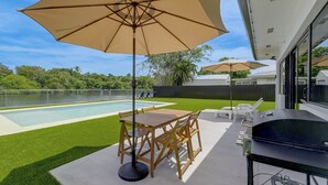 A backyard with a pool, a wooden table with chairs, and a barbecue grill. - Waterfront Hollywood Oasis w/ Private Pool! (Hollywood)
