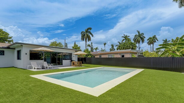 A backyard with a swimming pool, a patio with chairs, and a fenced area with palm trees. - Waterfront Hollywood Oasis w/ Private Pool! (Hollywood)