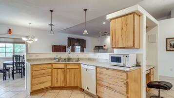 A kitchen with wooden cabinets, a built-in microwave, and a dining area with chairs.