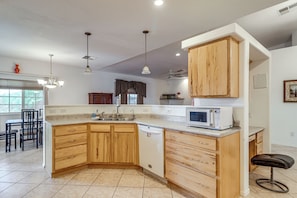 A kitchen with wooden cabinets, a built-in microwave, and a dining area with chairs. - Arizona City Monthly Rental w/ Yard & Workspaces (Arizona City)